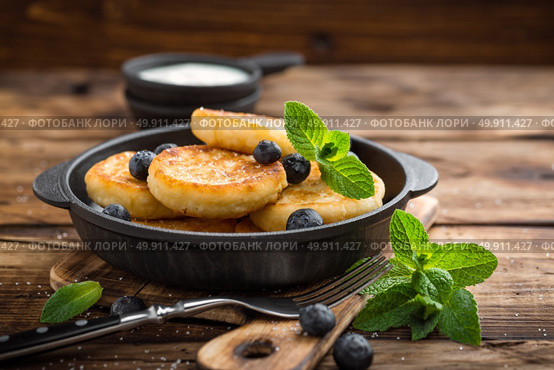 Delicious cottage cheese pancakes or syrniki with fresh blueberry in cast-iron pan on dark wooden rustic background, above view. Tasty breakfast. Стоковое фото, агентство Ingram Publishing / Фотобанк Лори