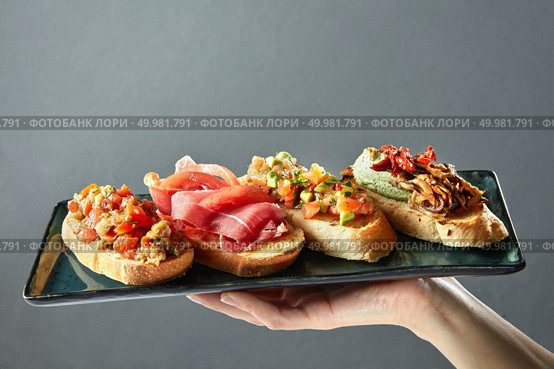 delicious variety of Italian bruschetta on a ceramic tray holds the hand of man. delicious variety of Italian bruschetta on a ceramic tray. Стоковое фото, агентство Ingram Publishing / Фотобанк Лори