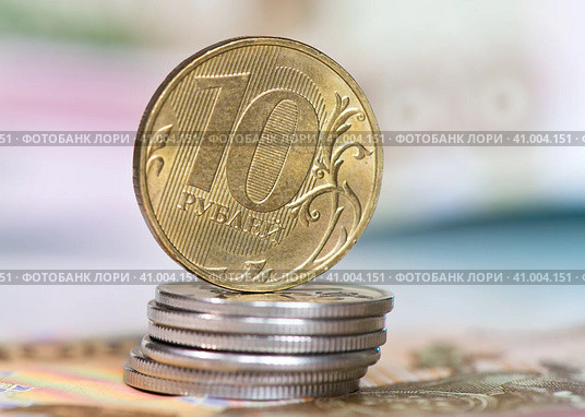 Деньги. Монета номиналом в 10 рублей на стопке монет в 1 рубль. На фоне 100-рублевых банкнот. Стоковое фото, фотограф E. O. / Фотобанк Лори
