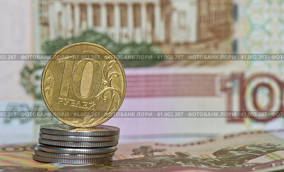 Деньги. Монета номиналом в 10 рублей на стопке монеток в 1 рубль на фоне 100-рублевых купюр. Стоковое фото, фотограф E. O. / Фотобанк Лори