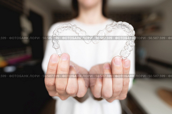 Dental care. Close-up of transparent aligners in the hands of a girl who is standing and showing a heart-shaped orthodontic device to the camera. selective focus.. Dental care. Close-up of transparent aligners in the hands of a girl who is standing and showing a heart-shaped orthodontic device to the camera. selective focus. Стоковое фото, агентство Ingram Publishing / Фотобанк Лори