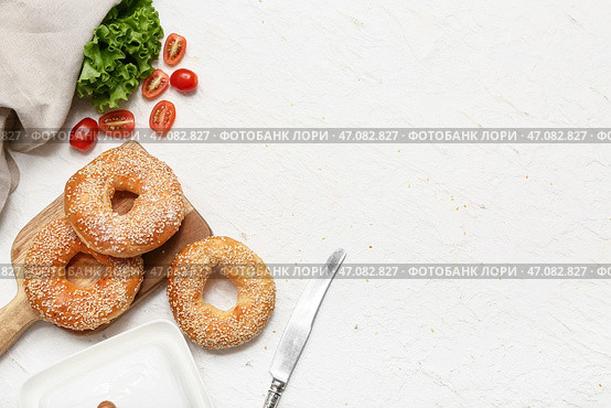Деревянная доска с вкусными бубликами с кунжутными семенами, свежим салатом и помидорами на белом фоне. Стоковое фото, фотограф Pixel_shot / Фотобанк Лори