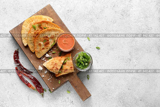Деревянная доска с вкусными чебуреками, соусом, зеленым луком и перцем чили на светлом фоне. Стоковое фото, фотограф Pixel_shot / Фотобанк Лори