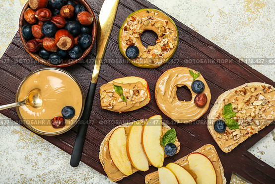 Деревянная доска вкусных бутербродов с ореховым маслом, яблоками, фундуком и черникой на светлом фоне, крупным планом. Стоковое фото, фотограф Pixel_shot / Фотобанк Лори