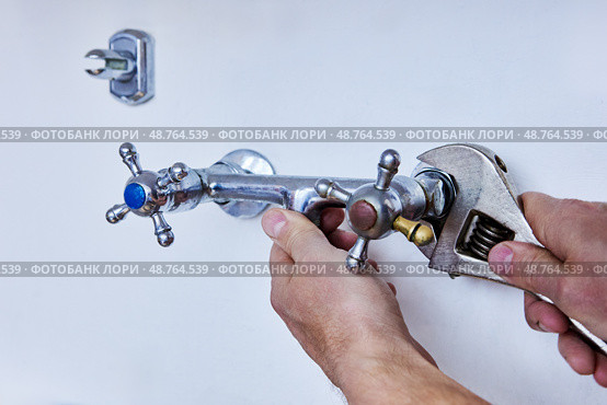 Detaching outdated faucet to install modern fixture, person uses wrench to unscrew metal tap with visible signs of use and colored handle indicators. Стоковое фото, фотограф Владимир Григорьев / Фотобанк Лори