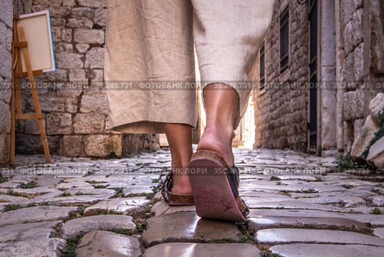 Detail shot of female legs wearing comfortable travel sandals walking on old medieval cobblestones street dring sightseeing city tour. Travel, tourism and adventure concept. Стоковое фото, фотограф Matej Kastelic / Фотобанк Лори