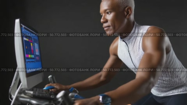 Determined senior athlete cycling on stationary bike with performance tracking software. Стоковое AI-видео, аниматор Юрий Поздников / Фотобанк Лори