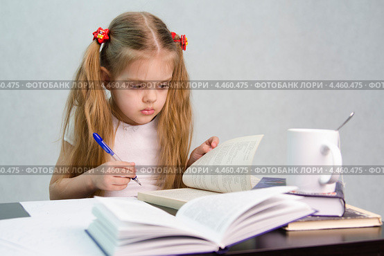 Девочка листает книгу и пишет на листе бумаги конспект сидя за столом. Стоковое фото, фотограф Иванов Алексей / Фотобанк Лори