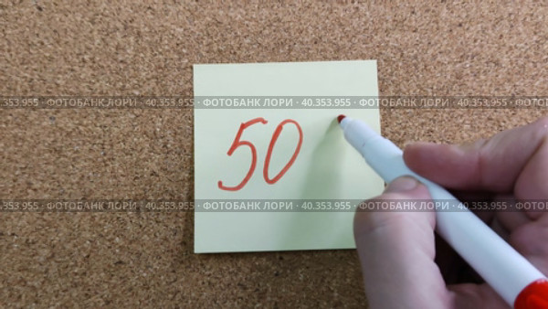 Девушка пишет надпись 50% красным маркером на желтом бумажном стикере, приклеенном к пробковой доске. Женская рука с цветным фломастером. Рукописный текст красивым почерком. Процент скидки, убытка или прибыли. Girl writes the inscription 50% with red marker on yellow paper sticker glued to cork board. Woman hand with colored felt-tip pen. Handwritten text in beautiful handwriting. Percentage of discount, loss or profit. Стоковое видео, видеограф Ирина / Фотобанк Лори
