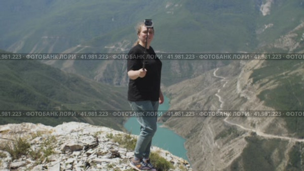 Девушка в черной футболке снимает себя на экшн-камеру, стоя на краю красивого каньона. Концепция путешествия с камерой. Стоковое видео, видеограф Воловодов Владимир / Фотобанк Лори
