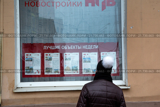 Девушка в шапке смотрит предложения по продаже недвижимости в витрине агентства недвижимости в центре города Москвы, Россия (2016 год). Редакционное фото, фотограф Николай Винокуров / Фотобанк Лори