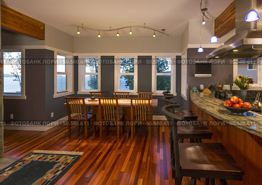 Dining room table and chairs and kitchen breakfast bar with wood floors, granite countertops, accent lighting and view windows in contemporary upscale home interior. Стоковое фото, агентство Ingram Publishing / Фотобанк Лори