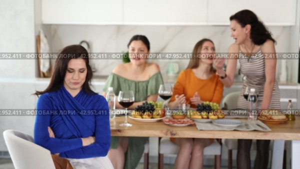 Displeased miffed young brunette sitting arms folded at house get-together, with female friends in background rebuking her, expressing dissatisfaction and disapproval. Стоковое видео, видеограф Яков Филимонов / Фотобанк Лори