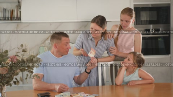 Dissatisfied woman screaming and demanding money from perplexed husband counting received salary at table in kitchen, two teenage girls standing nearby. Стоковое видео, видеограф Яков Филимонов / Фотобанк Лори