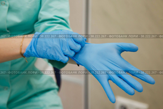 Doctor in dressing gown puts on sterile blue gloves. Concept of hero of doctors and stress. Concept of infection control. Risk of infection spreading. Copy space. Стоковое фото, фотограф Aleksandr Golubev / Фотобанк Лори