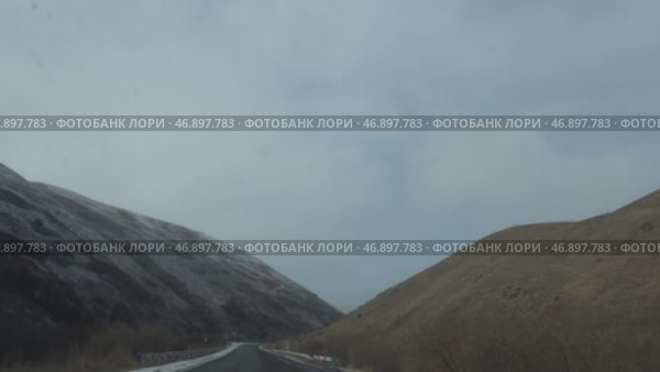 Дорога через горы: зима на пути из Армении в Грузию.   Зимний пейзаж горной дороги, соединяющей Армению и Грузию. Извилистая тропа проходит среди холмов, покрытых сухой травой, под серым зимним небом. Стоковое видео, видеограф Анна Чижова / Фотобанк Лори
