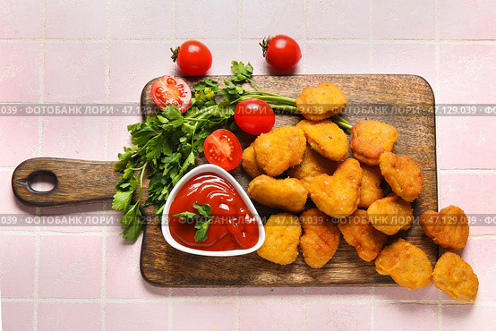 Доска с вкусными наггетсами, тарелкой кетчупа и петрушкой на столе, выложенном розовой плиткой. Стоковое фото, фотограф Pixel_shot / Фотобанк Лори