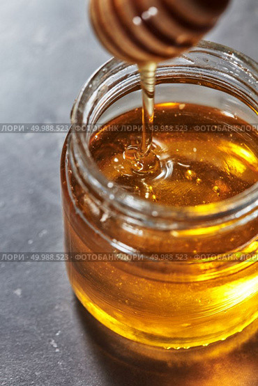 Dripping sweet honey into a glass pot of fresh organic syrup on a gray background. Jewish New Year healthy holiday concept. Traditional useful sweetness.. Organic sweet flower hohey dripping from stick into glass pot on a gray table. Rosh hashanah jewish New Year holiday. Стоковое фото, агентство Ingram Publishing / Фотобанк Лори