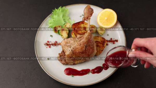 Duck leg confit with Brussels sprouts, baked potatoes, thyme, orange and lingonberry sauce. Traditional French cuisine. Woman pours sauce on a plate. Selective focus, close-up, black background. Стоковое видео, видеограф Наталья Любина / Фотобанк Лори