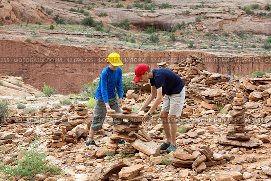 Два мальчика увлеченно строят пирамиды из камней. Poison Spider Mesa. Around the town of Moab, Utah, USA (2015 год). Стоковое фото, фотограф Ирина Кожемякина / Фотобанк Лори