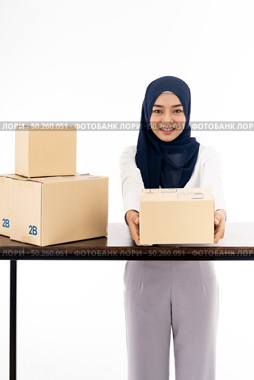 E-Commerce asian muslim women merchant work from home on wooden table with postal parcel cardboard boxes for shipping orders. Studio shot on white background for Selling online and small business SME. Стоковое фото, агентство Ingram Publishing / Фотобанк Лори