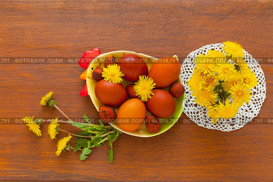 Easter composition with spring bouquet of yellow dandelion flowers on lace handmade napkin and painted red Easter eggs on chicken-shaped plate on wooden table. Flat lay, copy space, mock up, top view. Стоковое фото, фотограф Виктория Катьянова / Фотобанк Лори