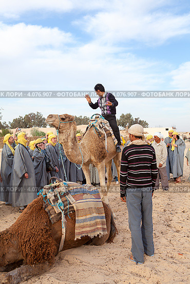 Экскурсовод показывает туристам как правильно сидеть на верблюде. Douz, Tunisia (2012 год). Редакционное фото, фотограф Кекяляйнен Андрей / Фотобанк Лори
