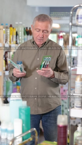 Elderly man holds several toothbrushes, carefully choosing them for his family. European buys dental hygiene products. Стоковое видео, видеограф Яков Филимонов / Фотобанк Лори