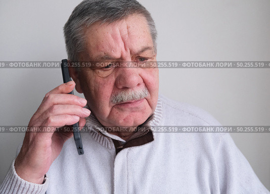 Elderly man is talking on a smartphone. A tired, distrustful, shocked pensioner who feels uncomfortable listening to an unknown caller making questionable requests. Стоковое фото, фотограф Терехова Марина / Фотобанк Лори