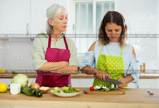 Elderly mother teaching adult daughter how to cook vegetable salad in kitchen. Стоковое фото, фотограф Яков Филимонов / Фотобанк Лори