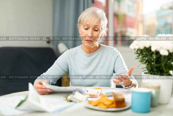 Elderly woman looking at papers at home, worrying about debts on bills. Стоковое фото, фотограф Яков Филимонов / Фотобанк Лори