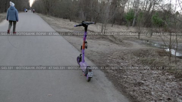 Электросамокат стоит на дорожке в лесу. Март. An electric scooter stands on a path in the forest. March. Редакционное видео, видеограф Горшков Александр / Фотобанк Лори