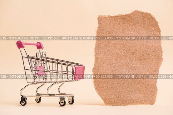 empty miniature shopping trolley near torn paper piece against colored backdrop. High resolution photo. empty miniature shopping trolley near torn paper piece against colored backdrop. High quality photo. Стоковое фото, агентство Ingram Publishing / Фотобанк Лори