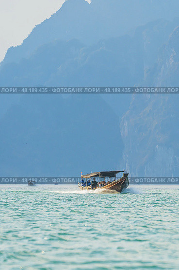 Enjoying a Scenic View of a Traditional Thai Boat Gracefully Navigating Through Serene Waters and Majestic Mountains in Thailand Lake travel. Стоковое фото, фотограф Владимир Разгуляев / Фотобанк Лори