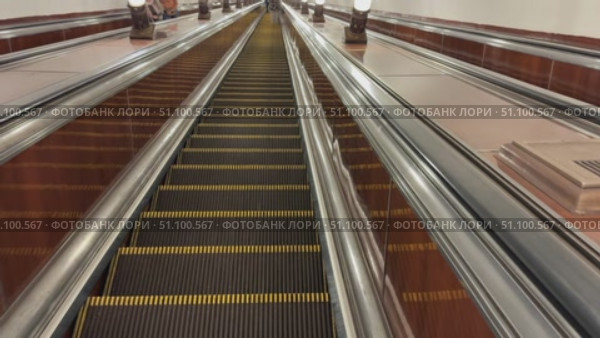 Escalator descending in metro station with polished metal surfaces and warm lighting reflections. Стоковое видео, видеограф Анастасия Золотницкая / Фотобанк Лори