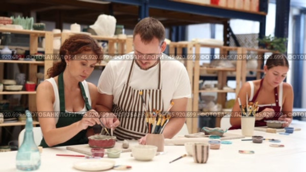 Experienced potter helps students learn how to make patterns on ceramic plates using paint and brush in a pottery workshop. Стоковое видео, видеограф Яков Филимонов / Фотобанк Лори