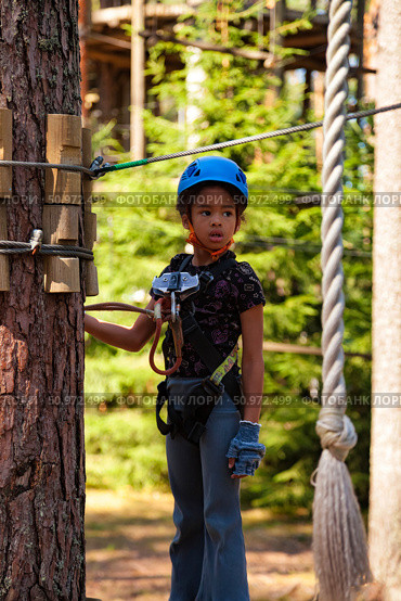 Exploring the Adventure Park, a Young Girl Prepares for a Thrilling Rope Challenge in Nature. Редакционное фото, фотограф Aleksandr Golubev / Фотобанк Лори