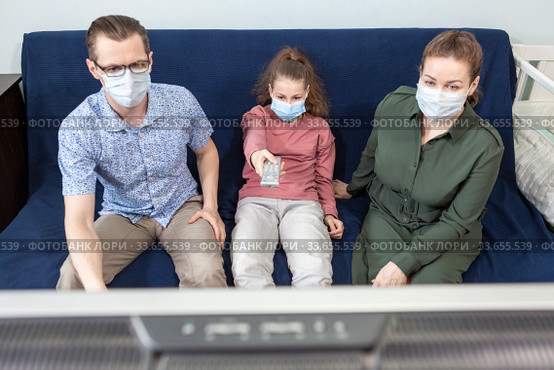 Family self-isolation, people staying at home, watching television, Caucasian father, mother and preteen age daughter sitting on sofa. Стоковое фото, фотограф Кекяляйнен Андрей / Фотобанк Лори