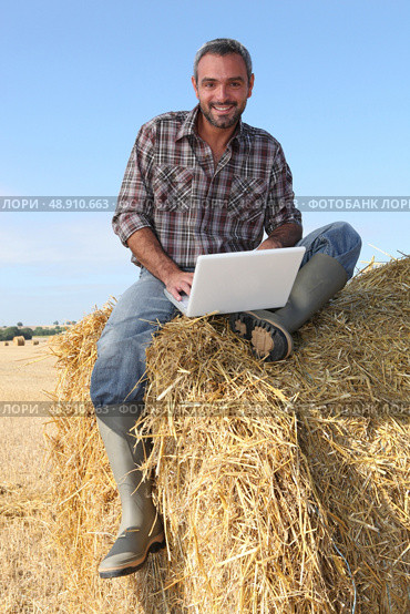 farmer seated on straw bale and doing computer. Стоковое фото, агентство Ingram Publishing / Фотобанк Лори