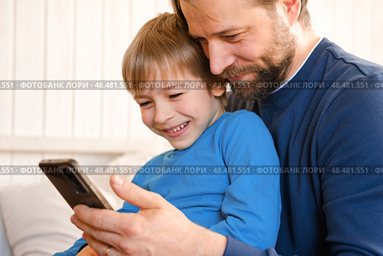 Father and son little boy laughing and using phone. They watching funny videos together, playing games on smartphone. Concept technology, smart phone addicted. Fun weekend activity. Modern fatherhood. Стоковое фото, фотограф Марина Демидюк / Фотобанк Лори