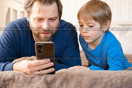 Father and son little boy laughing and using phone. They watching funny videos together, playing games on smartphone. Concept technology, smart phone addicted. Fun weekend activity. Modern fatherhood. Стоковое фото, фотограф Марина Демидюк / Фотобанк Лори