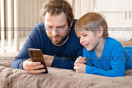 Father and son little boy laughing and using phone. They watching funny videos together, playing games on smartphone. Concept technology, smart phone addicted. Fun weekend activity. Modern fatherhood. Стоковое фото, фотограф Марина Демидюк / Фотобанк Лори