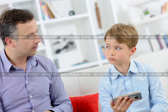 Father scolding young boy holding electronic device. Стоковое фото, агентство Ingram Publishing / Фотобанк Лори
