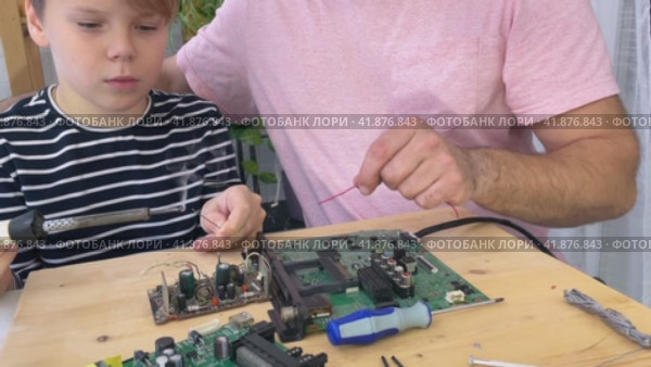 Father with his son spend time together. Close-up of a man teaching his boy at home to solder computer spare parts. Education moment during parenthood. Togetherness concept. Стоковое видео, видеограф Ирина Старикова / Фотобанк Лори