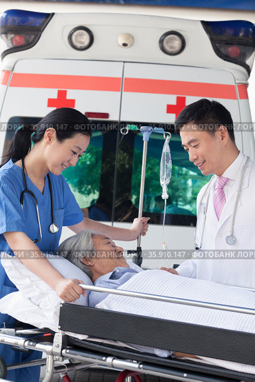 Female paramedic and doctor wheeling in a elderly patient on a stretcher in front of an ambulance. Стоковое фото, агентство Ingram Publishing / Фотобанк Лори