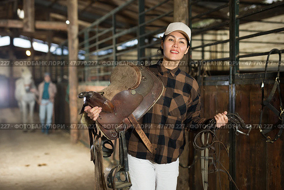 Female rancher carrying horse tack and saddle in horse farm. Стоковое фото, фотограф Яков Филимонов / Фотобанк Лори
