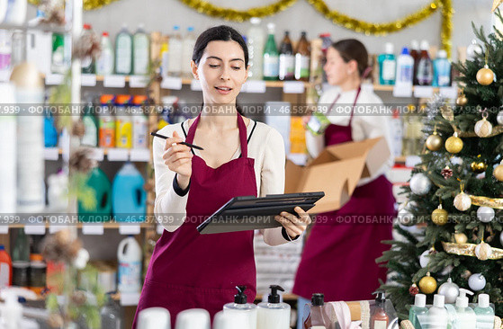 Female seller restocking using tablet while other is working in background. Стоковое фото, фотограф Яков Филимонов / Фотобанк Лори