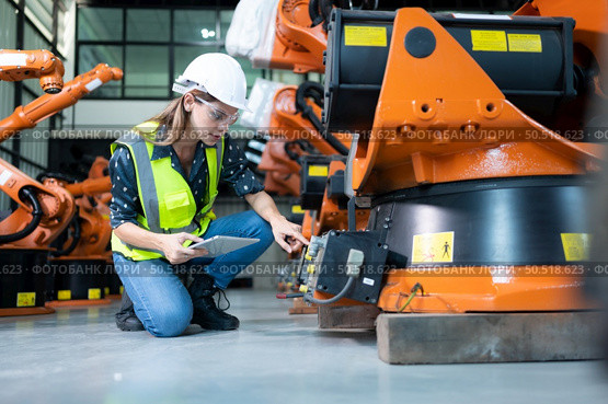 Female Technician Inspecting and repairing robotics arm in robots hangar and test the operation of the machine after being used for a while, as well as updating the software and calibration. Стоковое фото, агентство Ingram Publishing / Фотобанк Лори