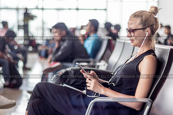 Female traveler using her cell phone while waiting to board a plane at departure gates at asian airport terminal. Стоковое фото, фотограф Matej Kastelic / Фотобанк Лори