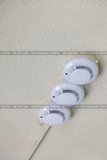 Fire detectors on ceiling. Smoke and fire detector in grey on grey wall. Triple smoke detector on textured ceiling. Vertical background with space for your lettering or logo. Стоковое фото, фотограф Aleksandr Golubev / Фотобанк Лори